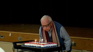White haired man blows out candles on cake