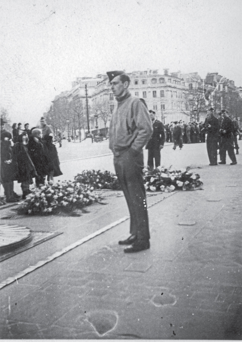 soldier stands in front of several piles of flowers left on the ground