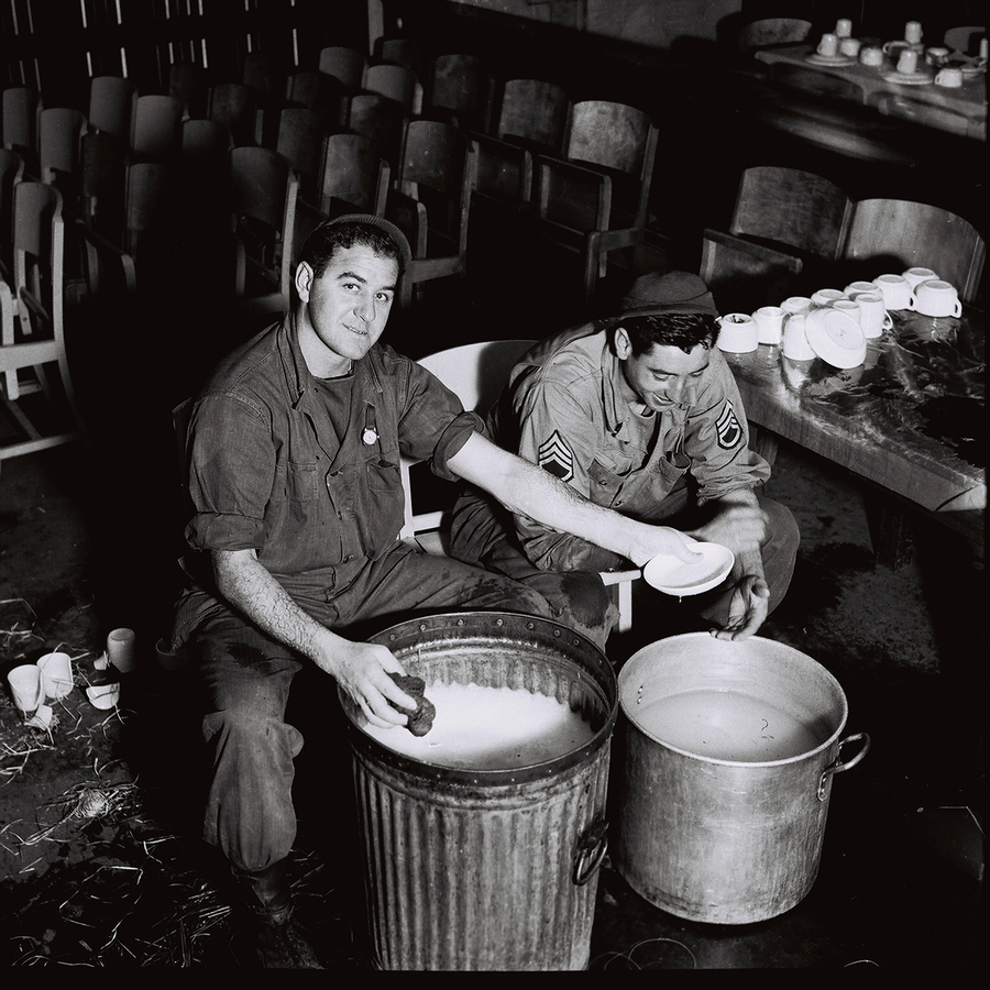 Two men washing dishes using metal cans for the water