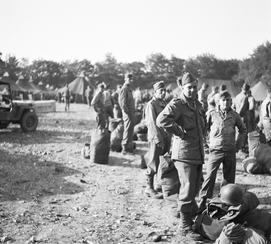 Soldiers lined up outside tents with their belongings on the ground in front of them