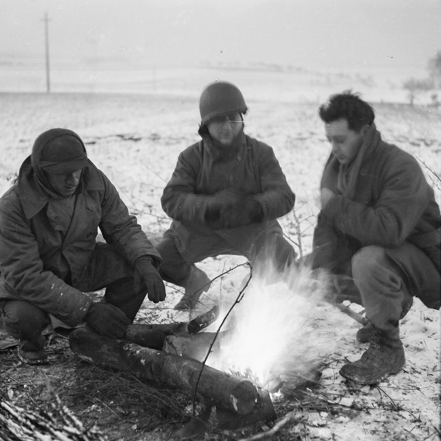 Three soldiers crouched near a fire with snow on the ground