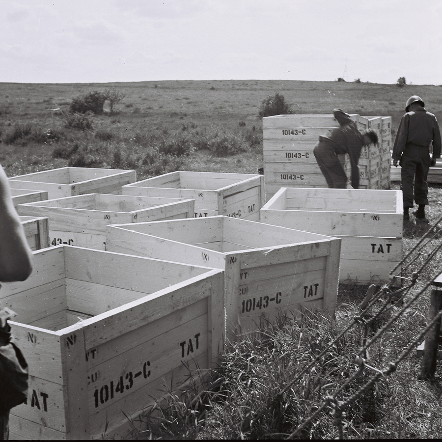 Men handling large wooden crates in an open field