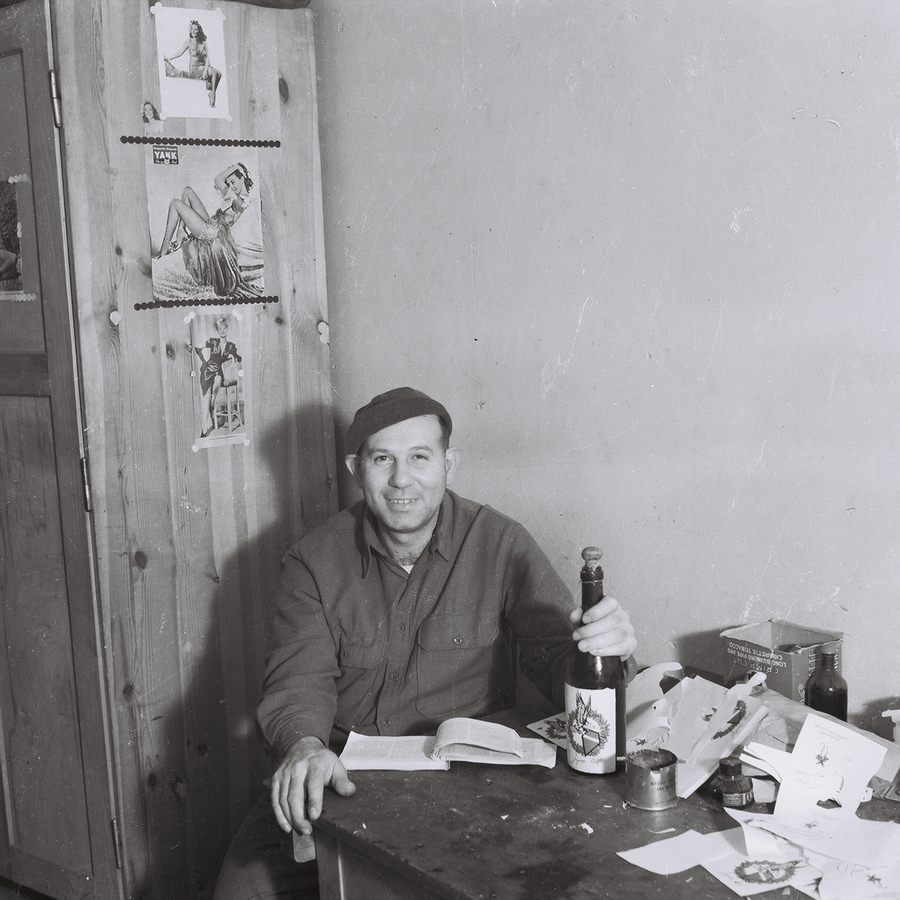 Man seated with a bottle of liquor in front of girly calendar images