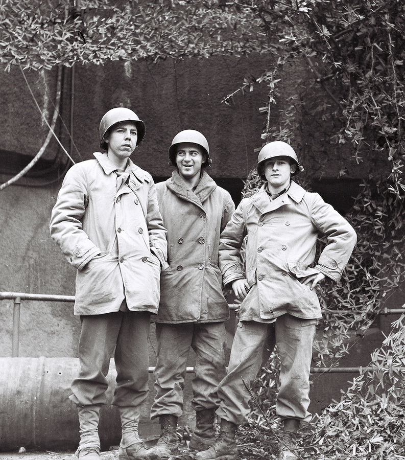 Three soldiers standing in front of a building and plant growth