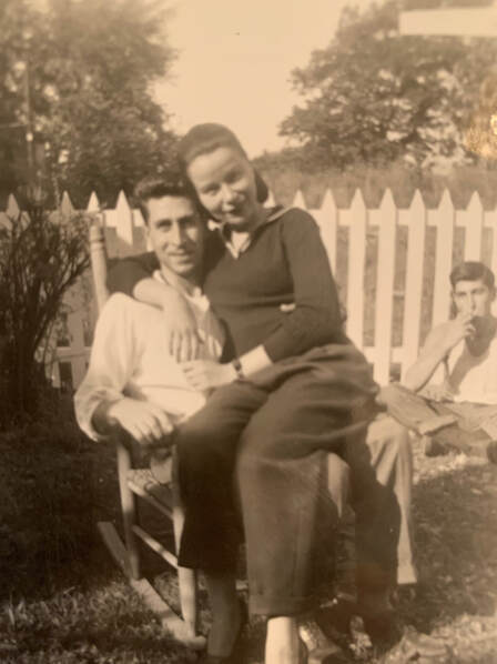 man seated in a rocking chair outside on a lawn with a woman seated in his lap