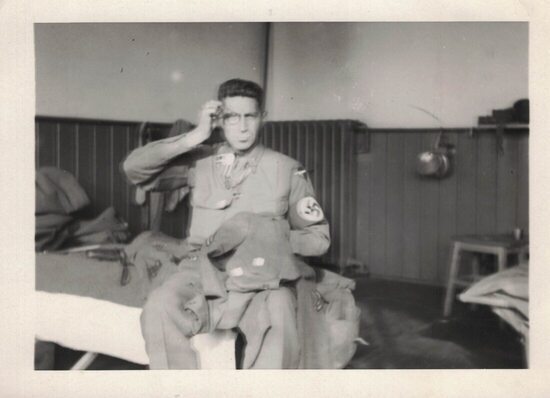 uniformed man sitting on a bunk wearing a Nazi arm band and carrying some clothing