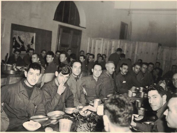 many soldiers on two long tables eating dinner indoors