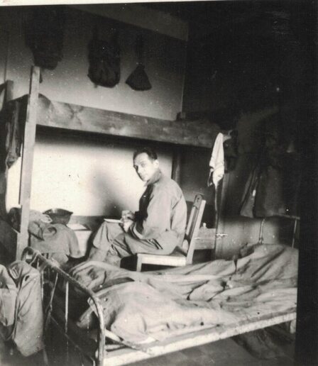 man sitting in a chair next to bunk beds writing a letter
