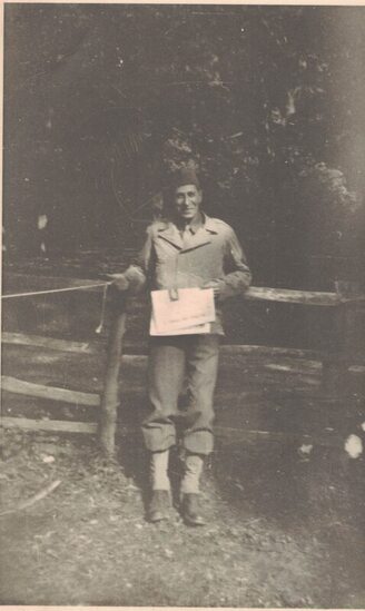 uniformed man leaning against a fence with a newspaper in his hands