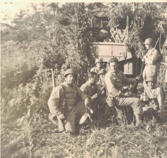 group of uniformed men in tall grass near a vehicle