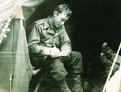 uniformed man seated in a tent writing a letter