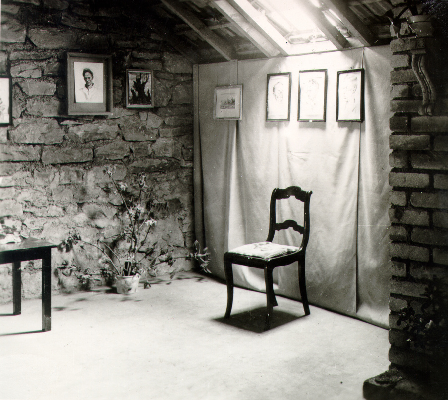 a chair under a skylight in a stone room with art hanging on the walls