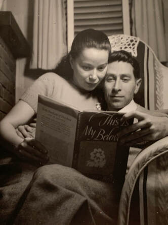 a woman sitting on a man's lap in an armchair, reading a book together