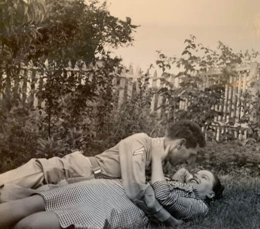 uniformed man and a woman in a dress lying down on a grassy lawn and looking lovingly at each other